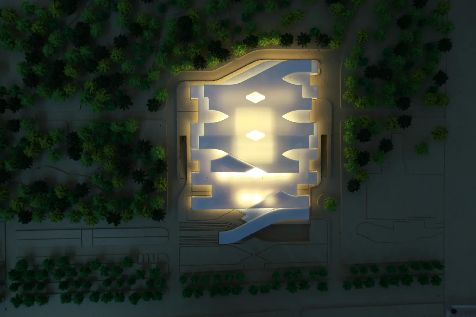 Lit physical model seen from above, showing the courtyards cut into the roof