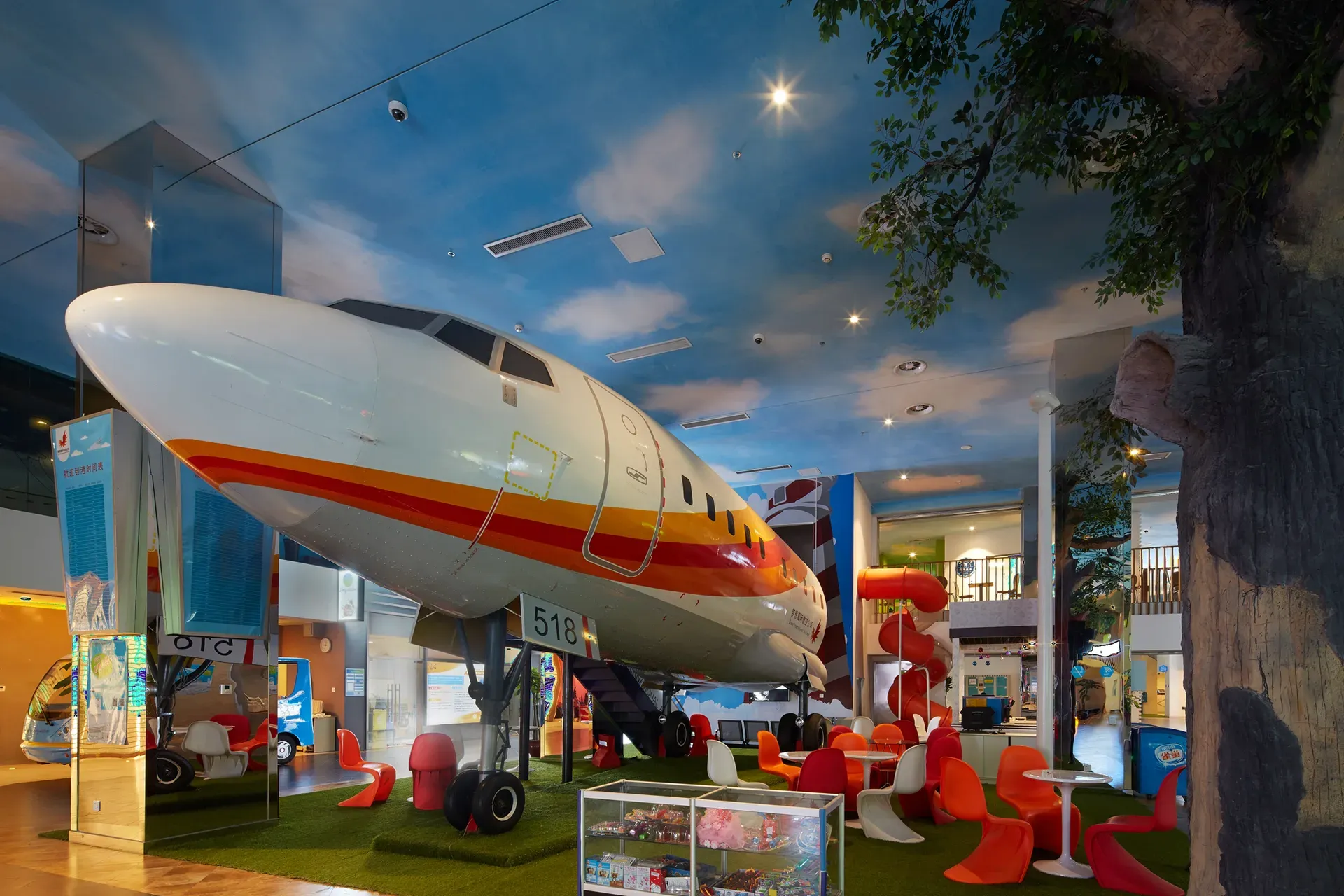 Aircraft fuselage set among play equipment under a ceiling painted as sky