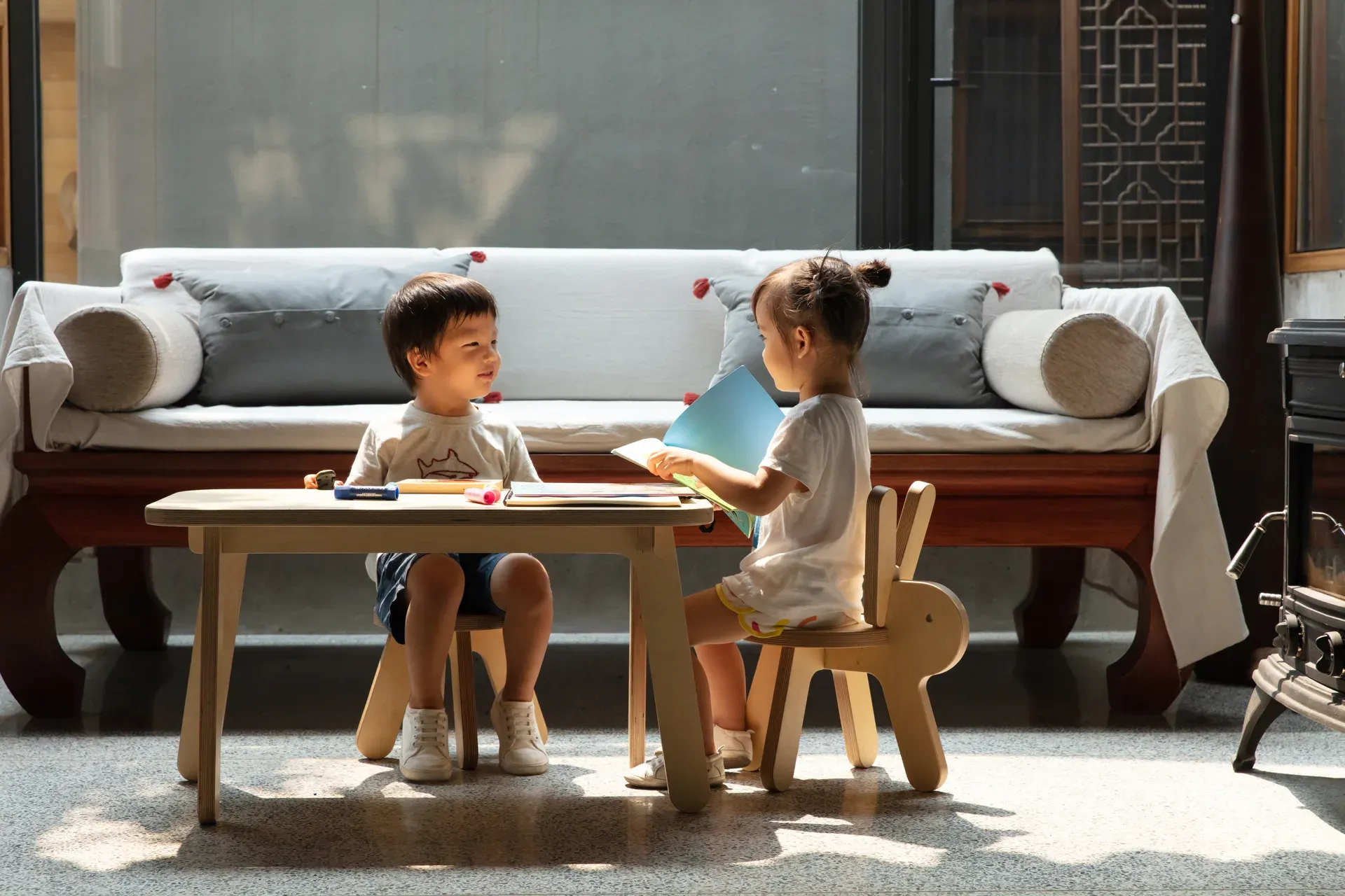 Two children reading at a low plywood table with an animal-shaped chair