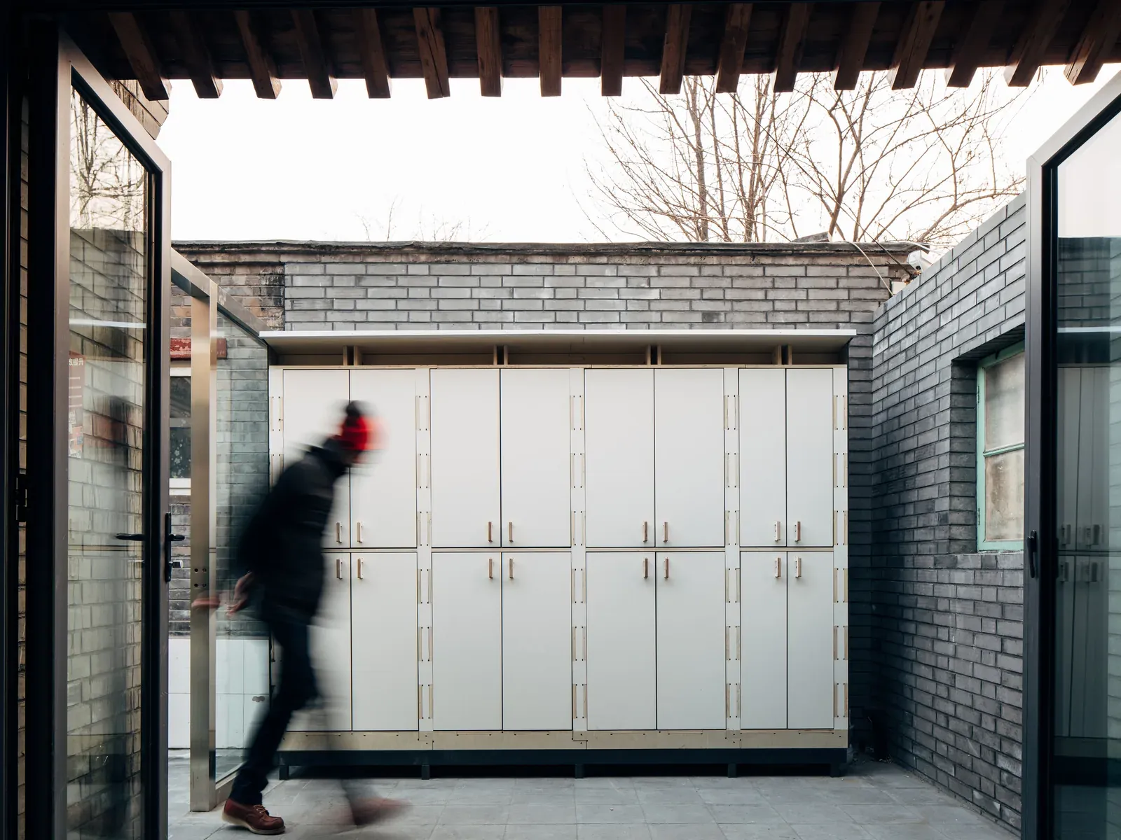 Storage modules along a courtyard wall, with a passer-by in motion